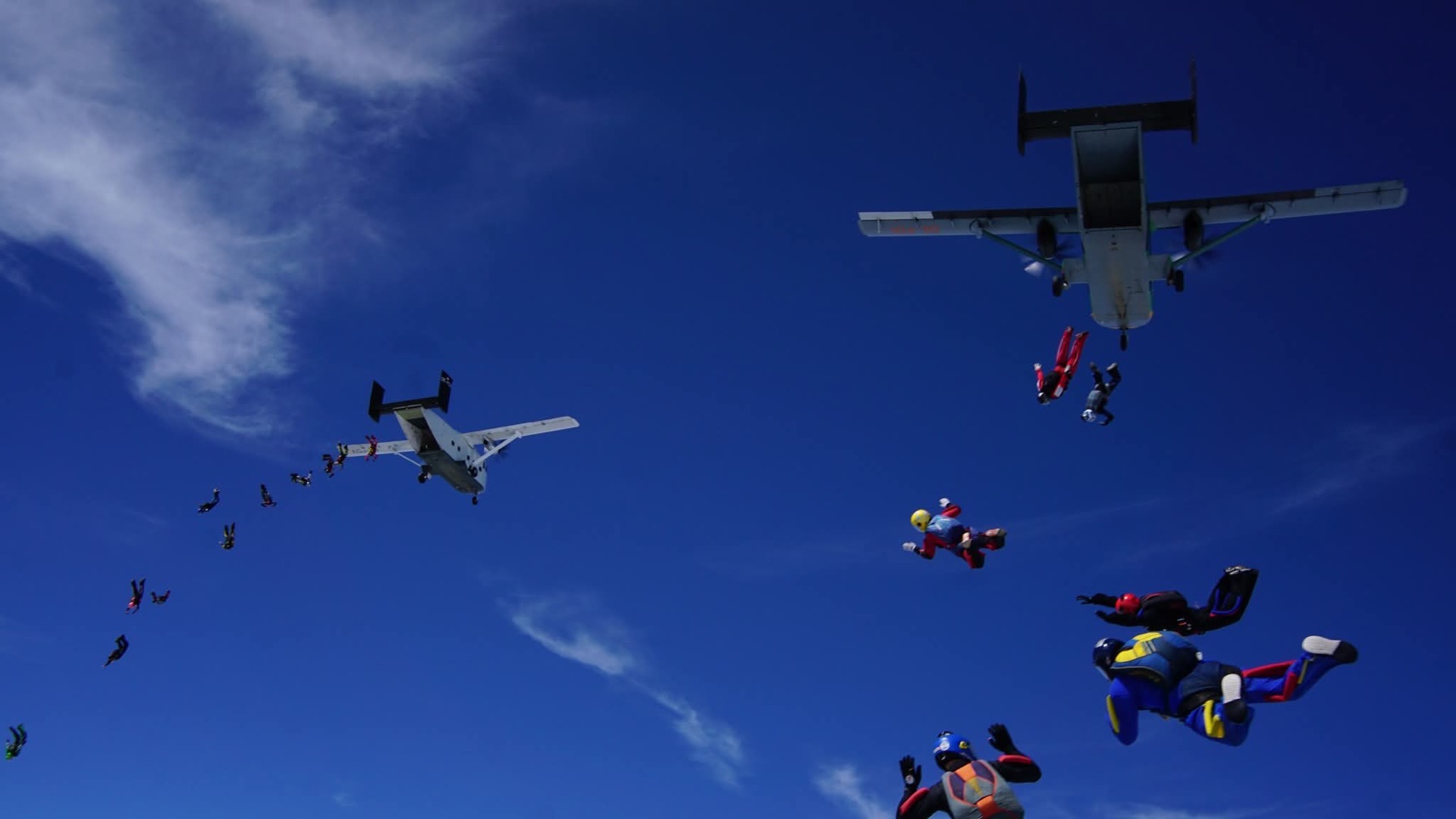 Two aircraft dropping skydivers in a line against a clear sky