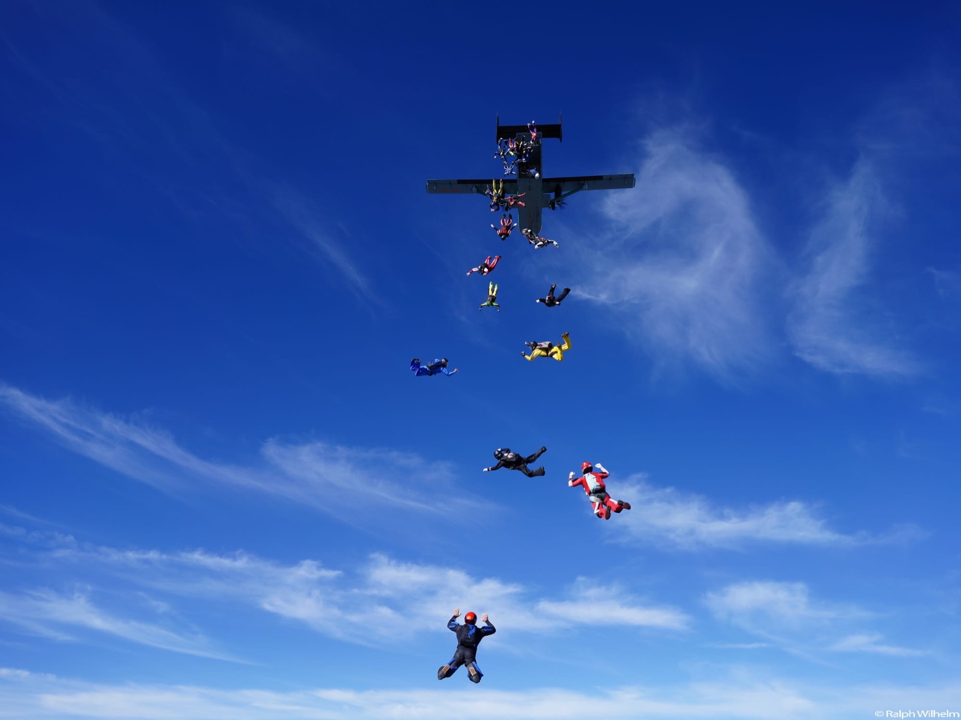 Skydivers exiting an aircraft in a line against a blue sky